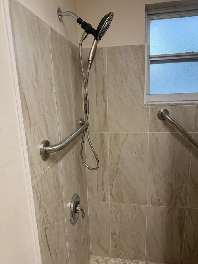 Close-up of a tiled shower wall with a handheld fixture, grab bar and window