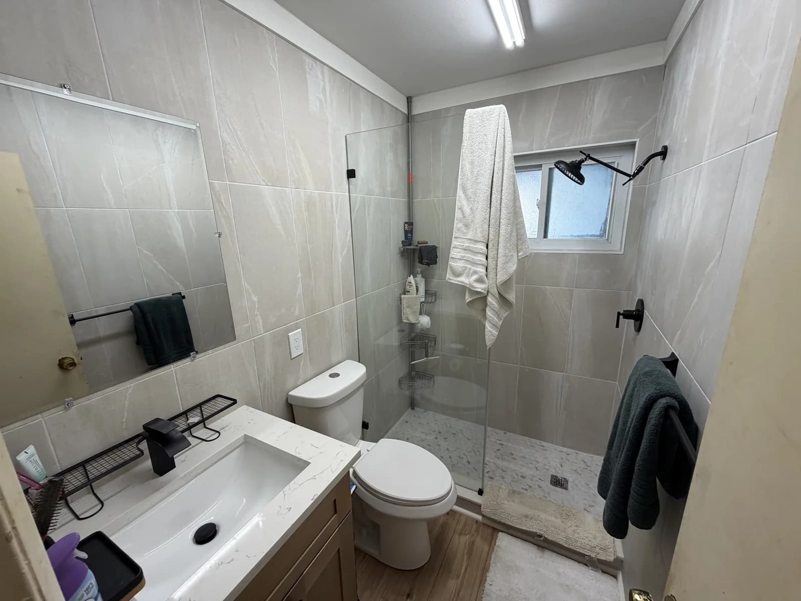 Remodeled bathroom with a large-format tiled shower, glass panel, floating wood vanity and black fixtures