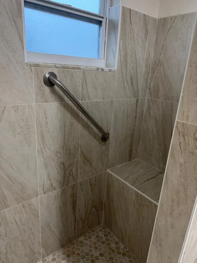 Close-up of a walk-in shower's tiled wall, grab bar and recessed window