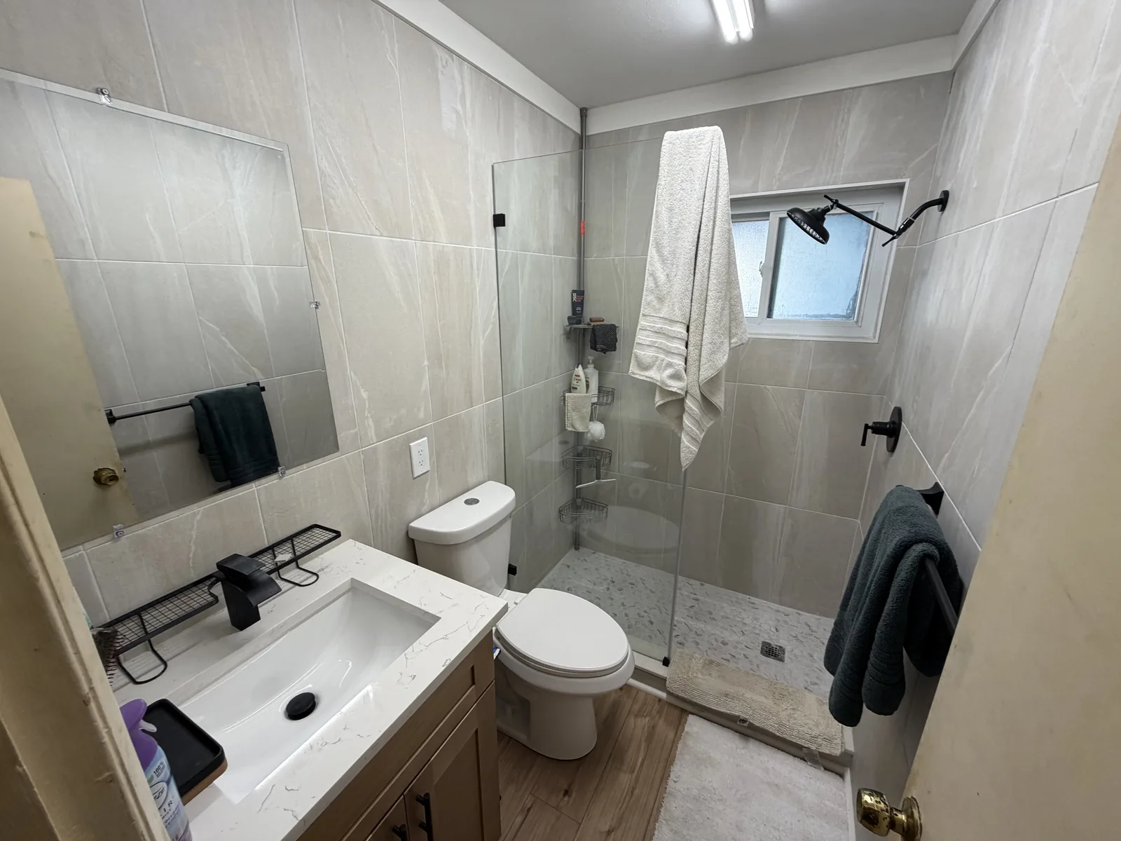 Walk-in shower with large-format tile, a glass panel and a low threshold, beside a floating vanity